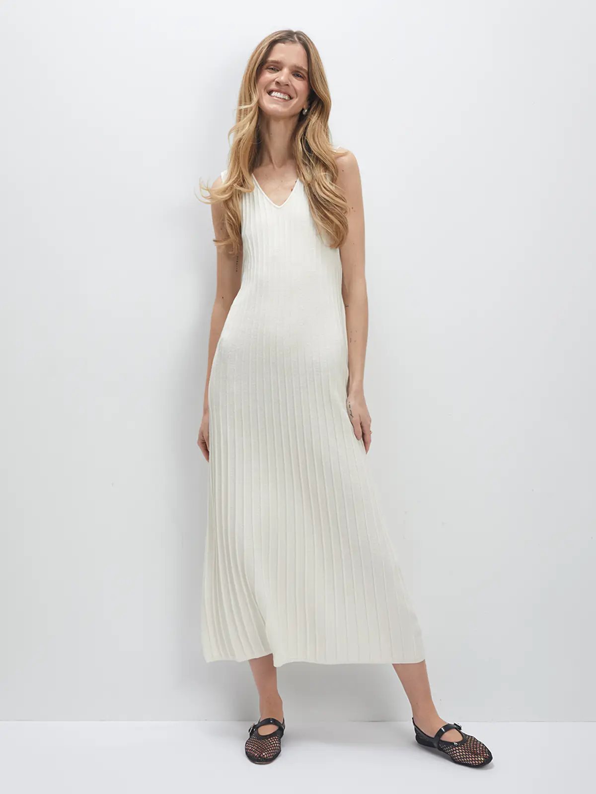 Model stands front-facing in the white JOCELYN V-neck sleeveless knit dress with pleated skirt and mesh flats.