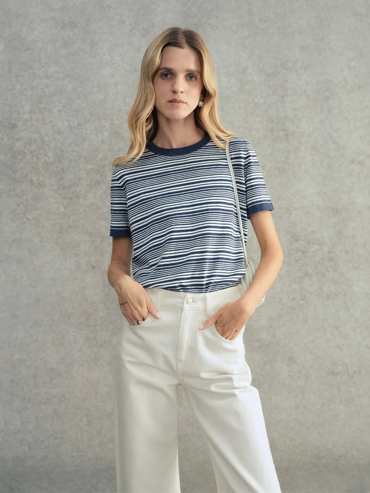 Model wearing navy striped JUSTINE t-shirt with white wide-leg trousers and small shoulder bag, hands in pockets
