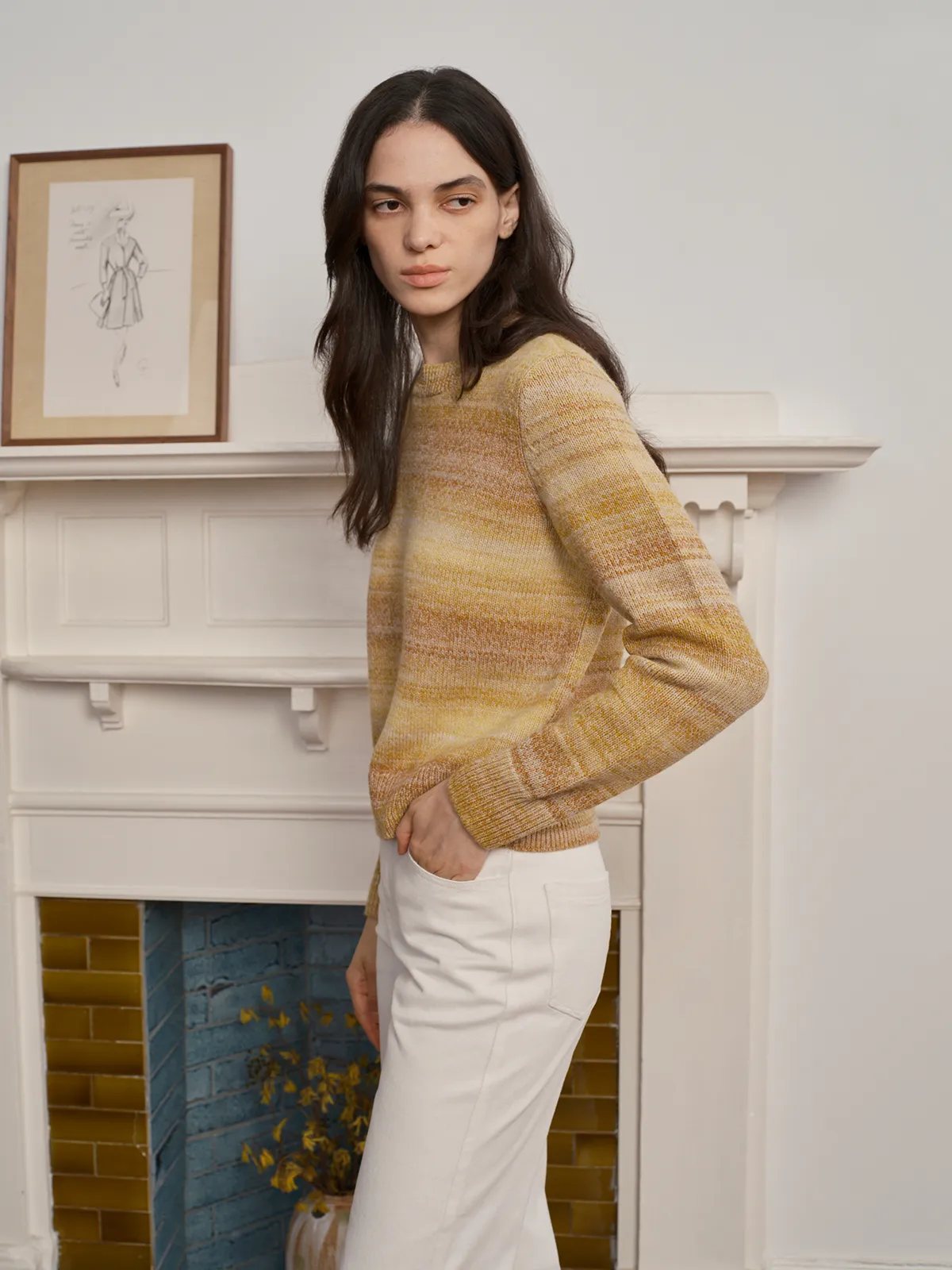 Model in TANYA Gradient Stripe Knit Vest paired with white flared trousers beside vintage fireplace