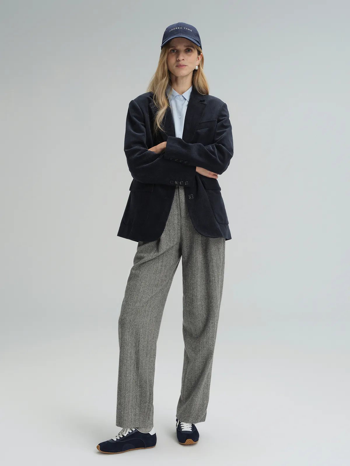 Front view of model wearing Gray wool herringbone tapered trousers with a dark blazer, light shirt, cap, and sneakers.