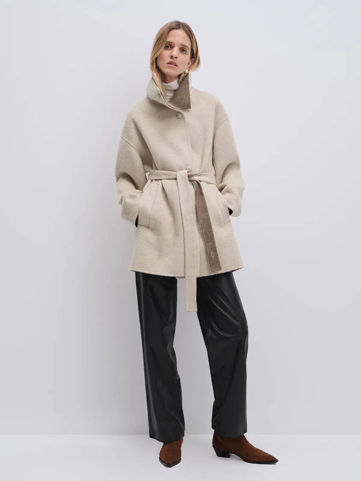 Model wearing the Oatmeal reversible two-tone long coat with belt tied, side view showing contrasting collar lining.