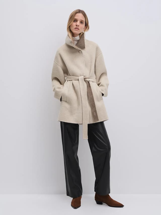 Model wearing the Oatmeal reversible two-tone long coat with belt tied, side view showing contrasting collar lining.
