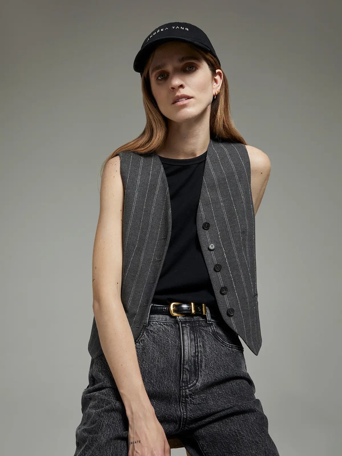 Grey pinstripe wool vest with five buttons, paired with a tee, dark jeans, and a cap.