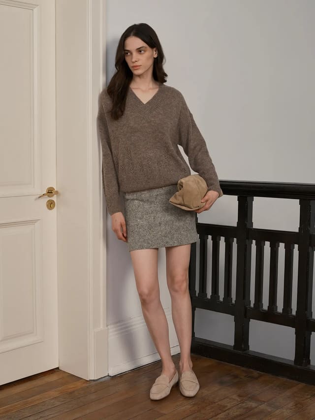 andreatang AIRY Relaxed Alpaca Blend Knit Jumper in taupe, styled with grey tweed mini skirt and beige loafers against white door and wooden floor