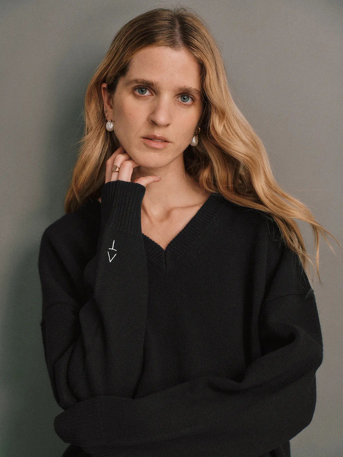 Side view of the Black CARRIE Merino Wool V-Neck Jumper worn with a pleated midi skirt and black loafers.