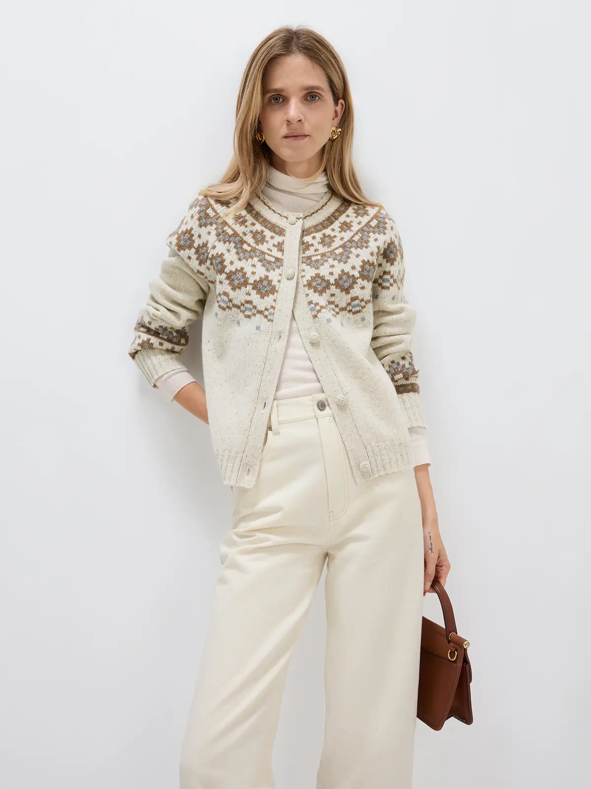 Model wearing an Oatmeal Fair Isle cardigan layered over a turtleneck and trousers, holding a small bag.