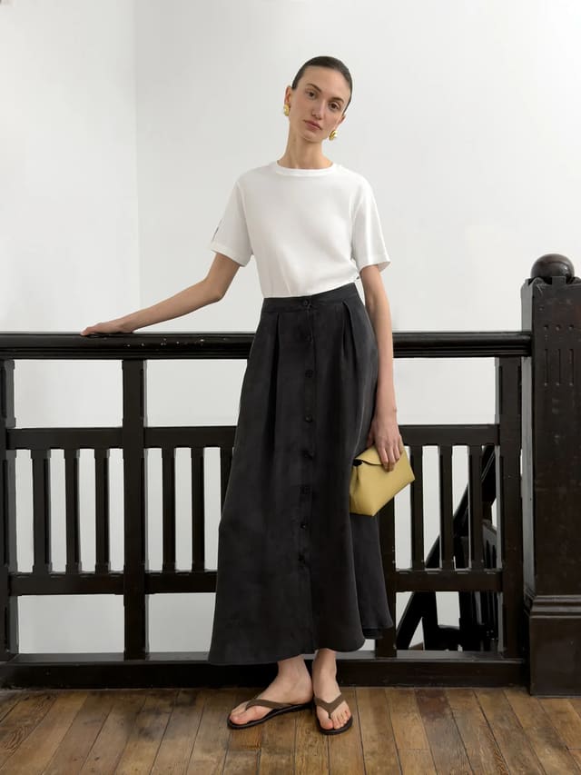Model wearing andreatang EDWARD white relaxed t-shirt with black button-front midi skirt, gold earrings, yellow clutch — Parisian chic minimalist outfit