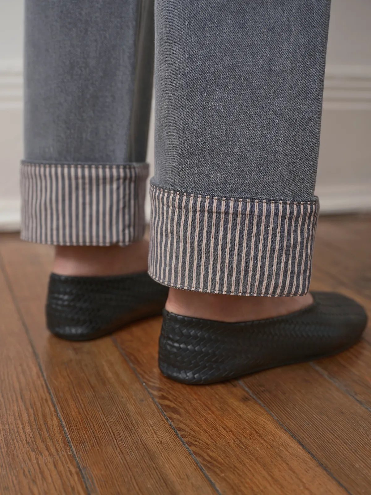 Low-angle detail of FLIPSIDE jeans cuffs and black woven leather flats on hardwood floor
