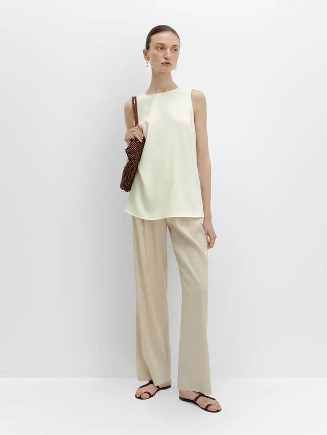 Side profile of FINN linen trousers with ivory sleeveless top and beaded bag