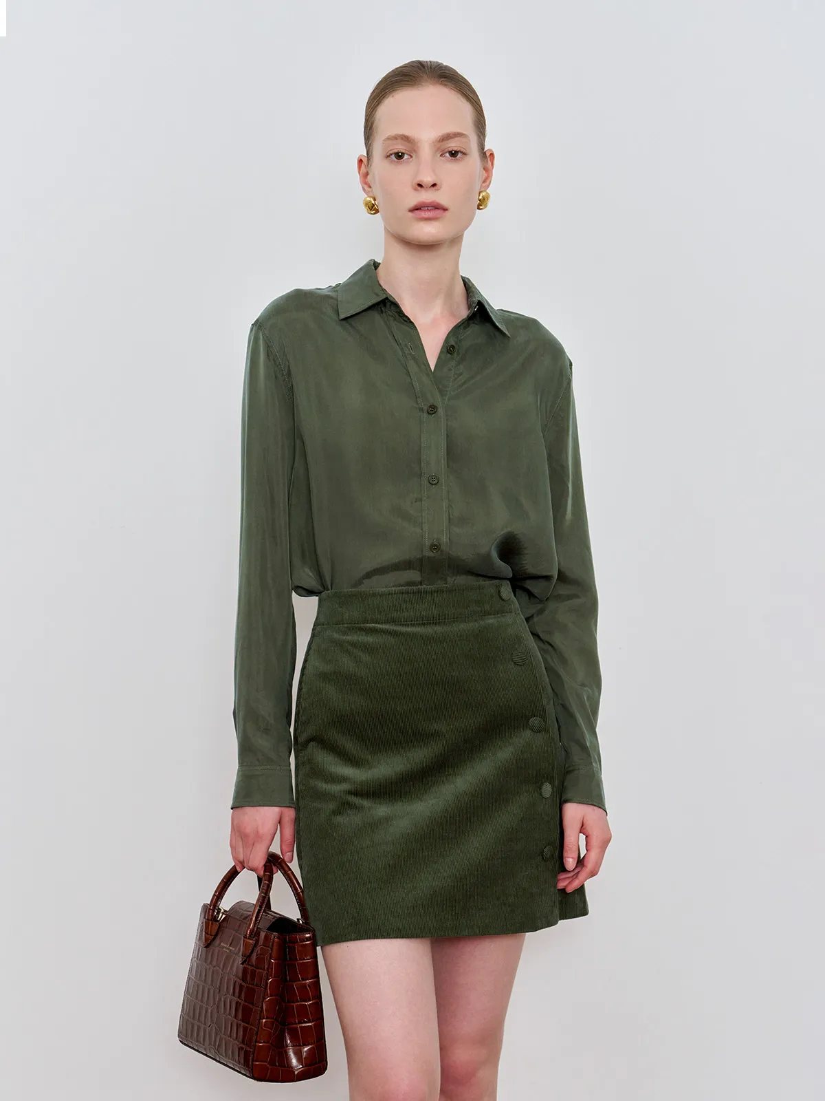 Front view of GREER olive cupro shirt with corduroy mini skirt and brown croc bag against white background
