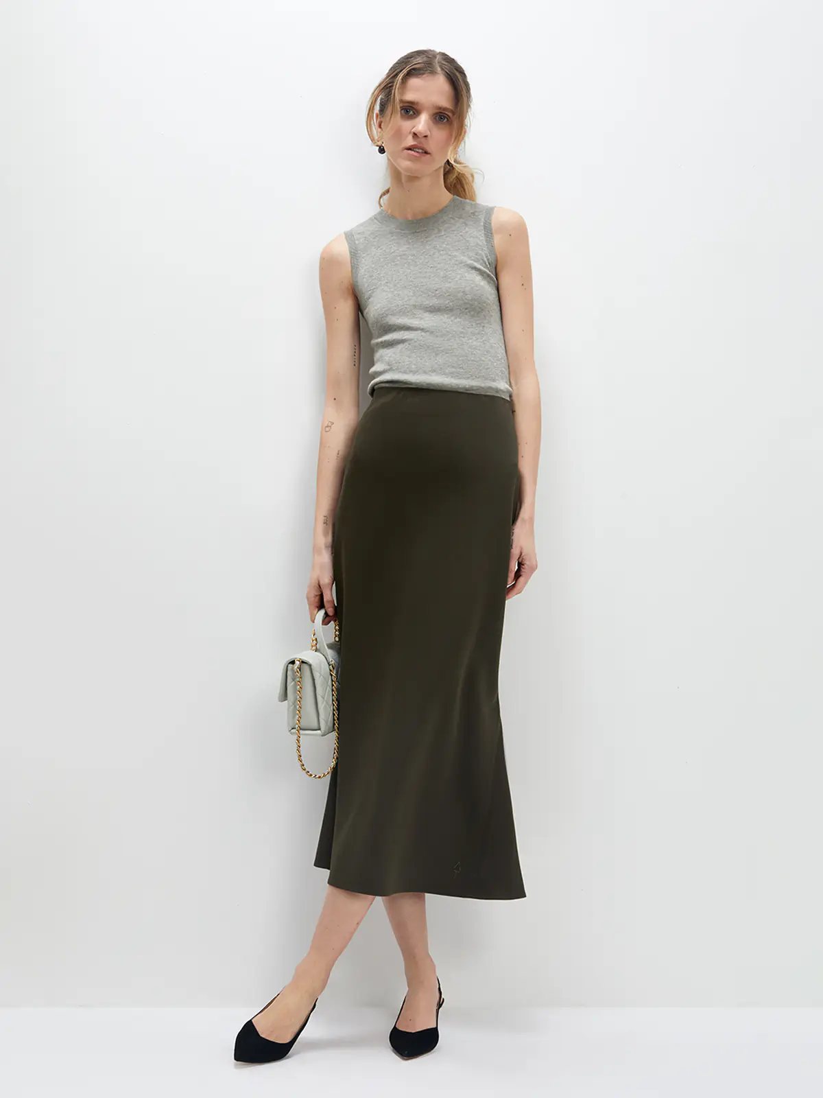 Model wearing an olive green acetate mermaid skirt with a sleeveless top, holding a small bag, front view.