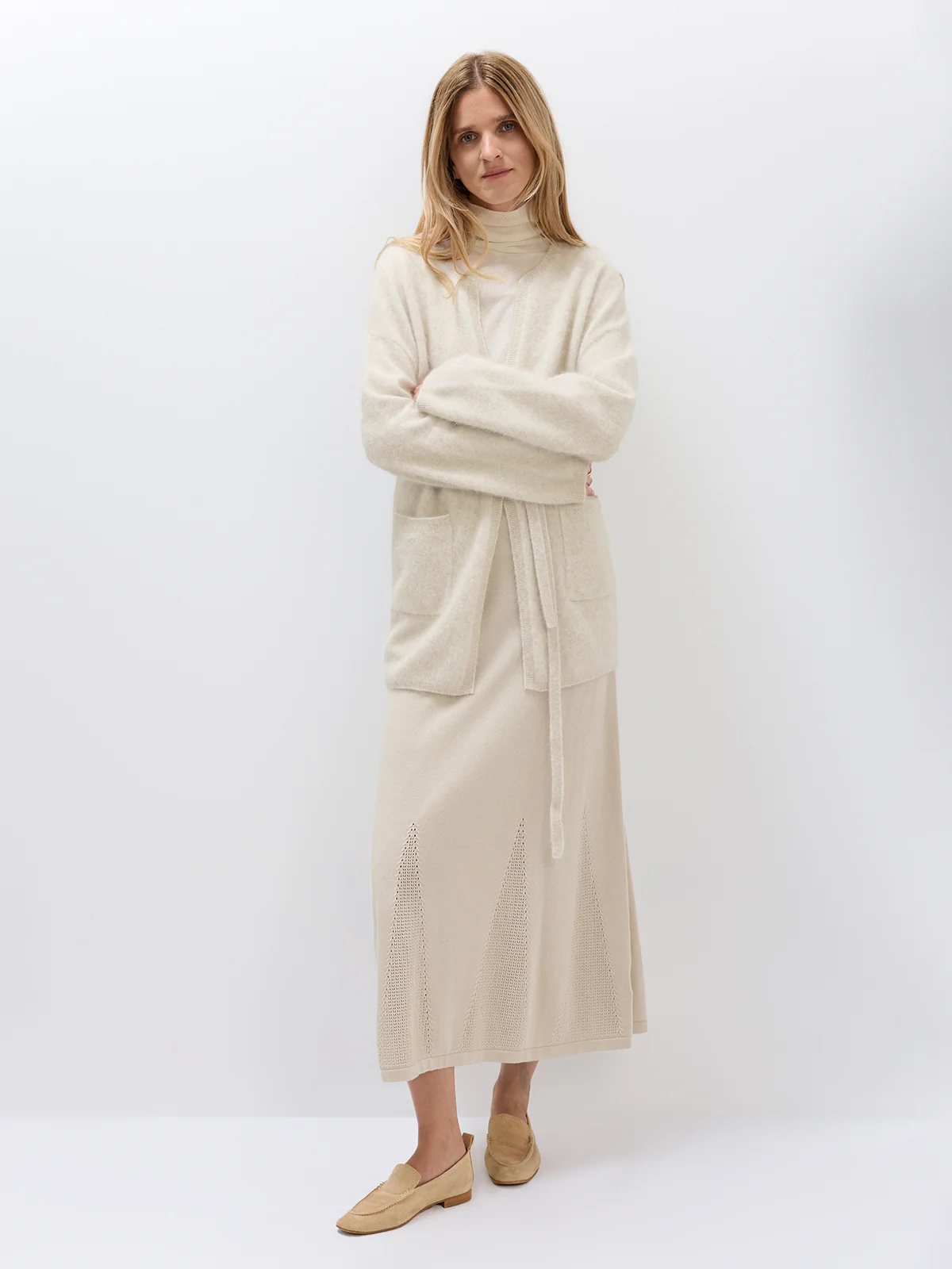 Model standing with arms crossed, wearing the Oatmeal belted cardigan over a matching knit set.
