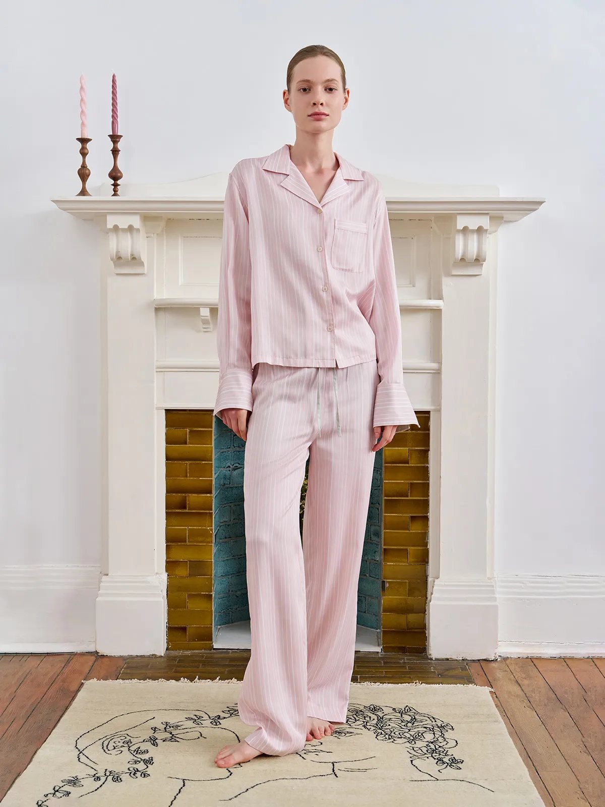 Front full-body portrait of model wearing LARISSA pajama set standing before fireplace, direct gaze