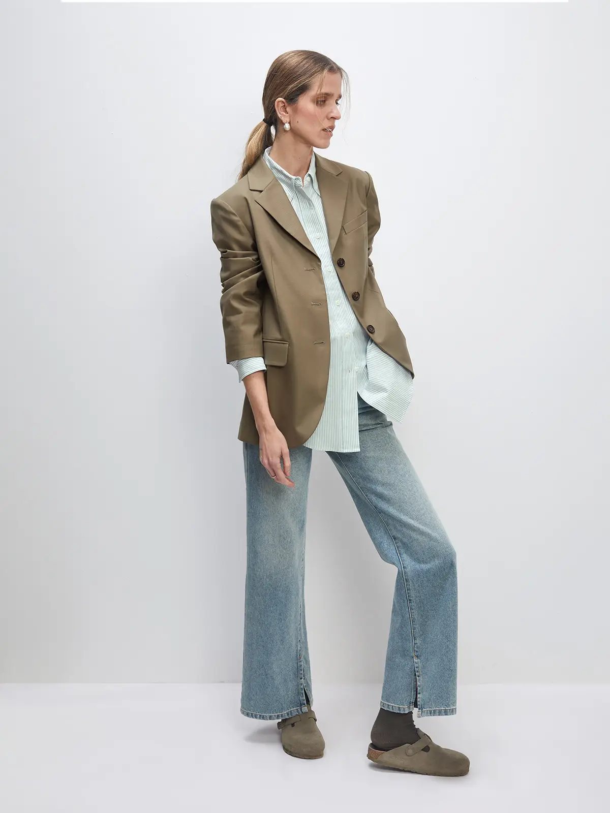 Model wearing blue retro washed split flared jeans with blazer, light shirt, and clogs, side pose.
