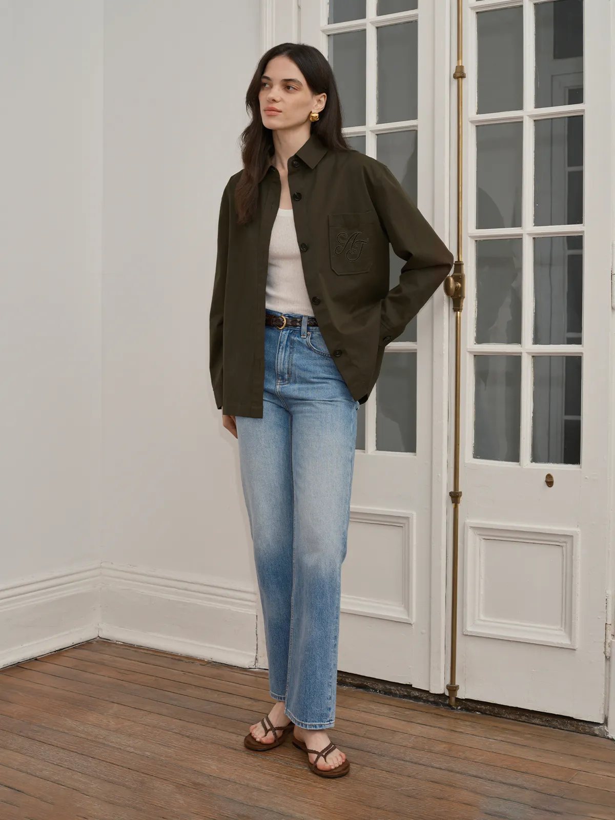 Model in olive HUCK jacket layered over cream ribbed top, paired with light-wash straight-leg jeans and brown sandals