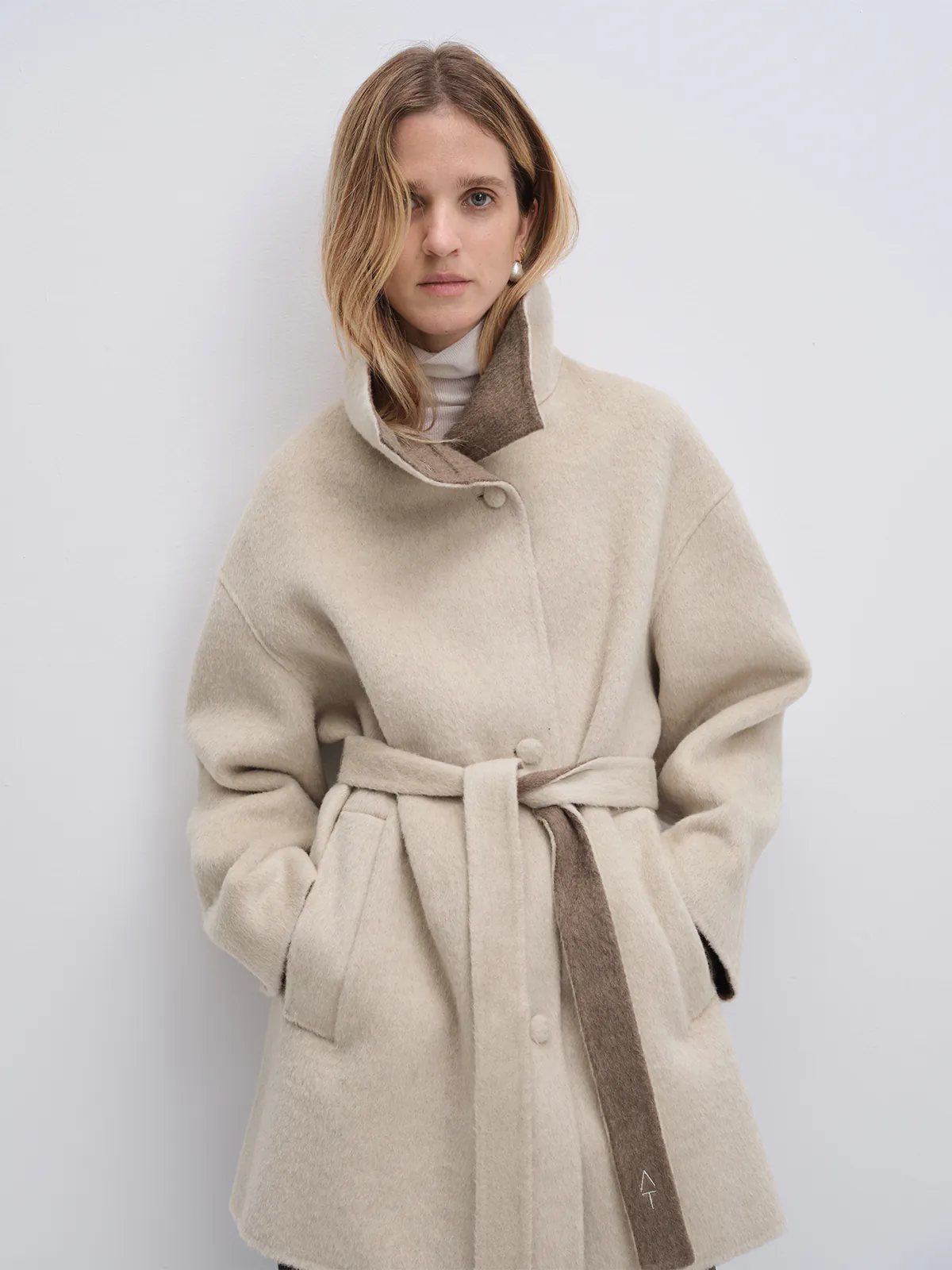 Front view of model wearing the Oatmeal reversible two-tone long coat open, revealing contrasting inner collar lining.