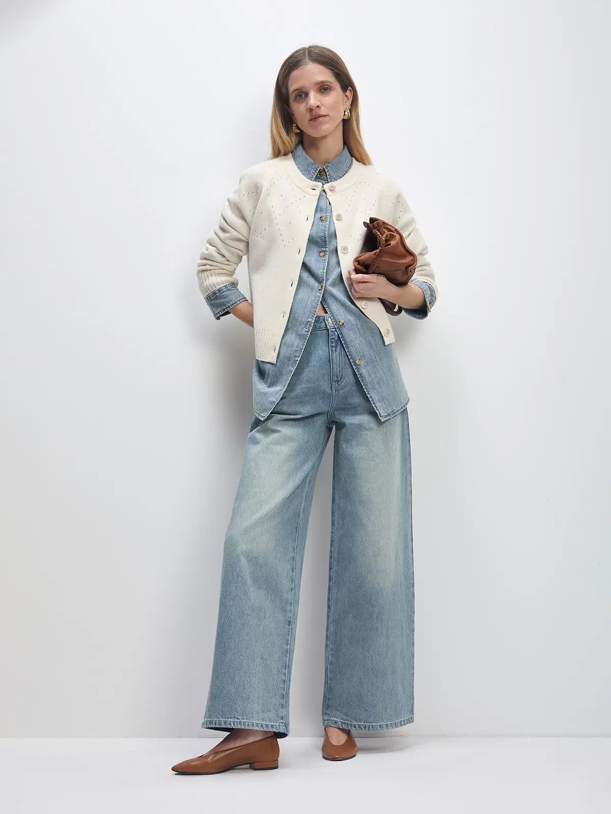 Model wearing the white Fair Isle hollowed knitted cardigan open over a denim shirt and wide-leg jeans, holding a clutch.