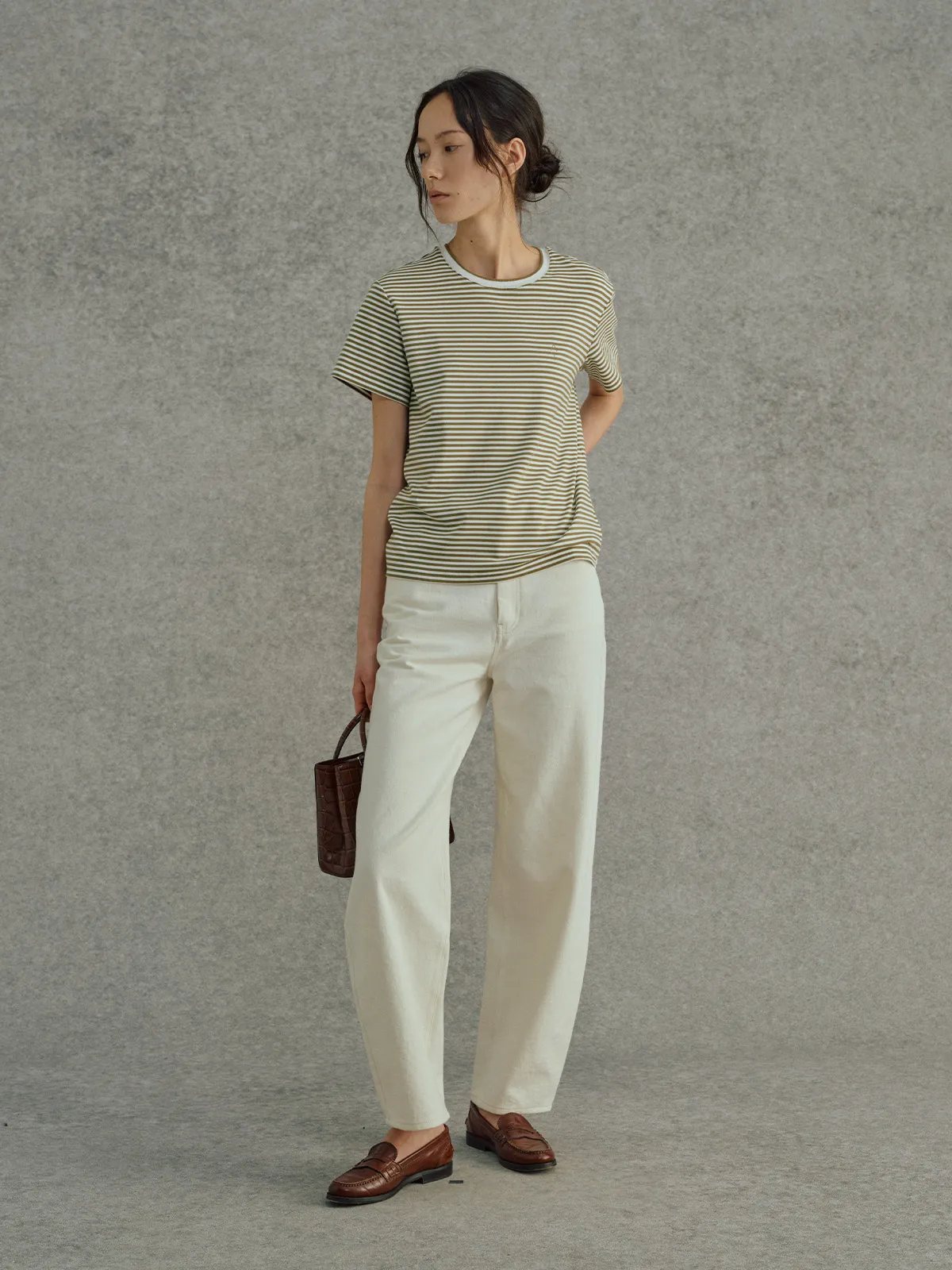 Model in FINLEY striped t-shirt with cream trousers and brown leather loafers, holding croc-embossed bag, three-quarter view