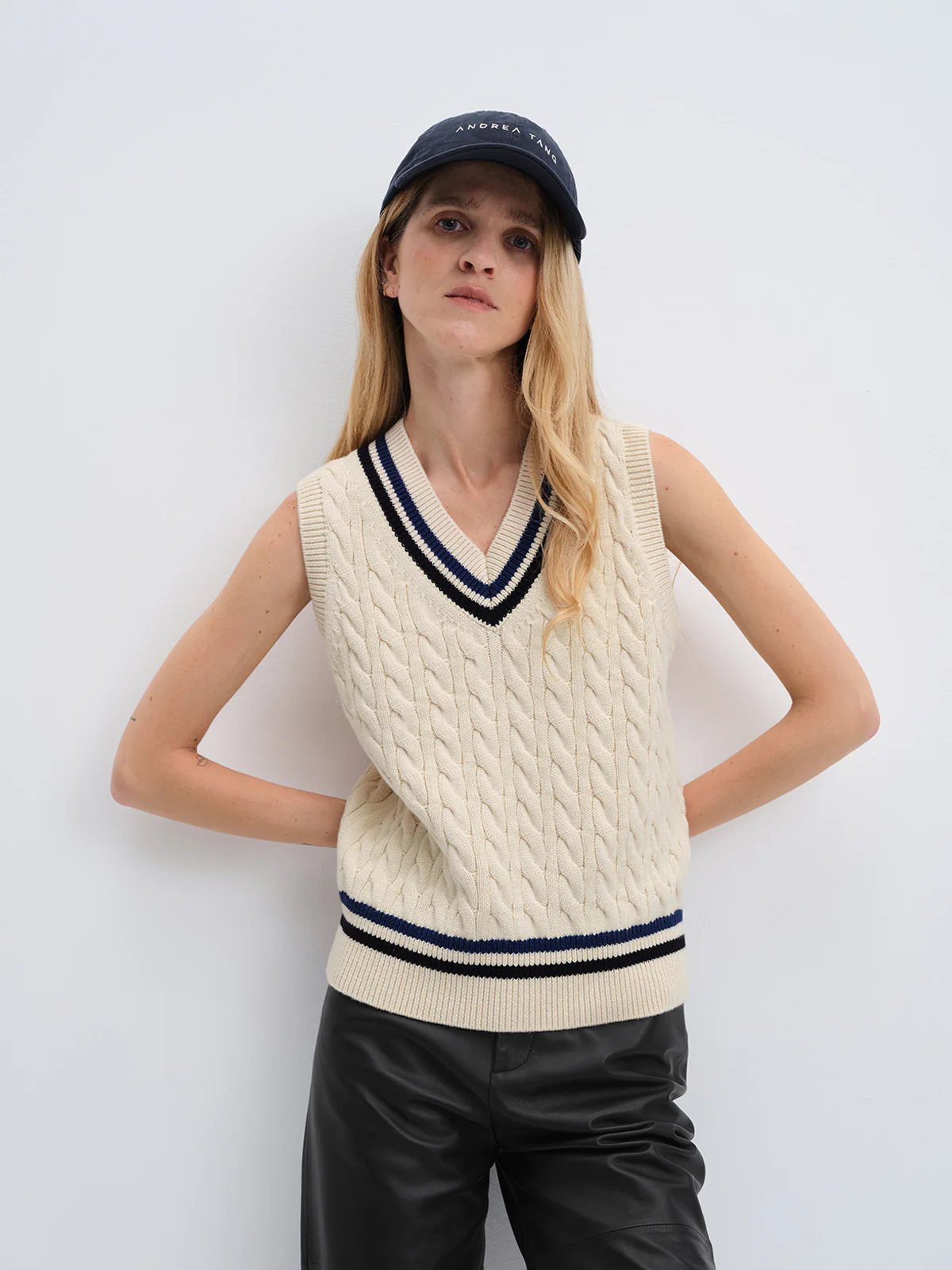 Close-up of andreatang cream cable-knit V-neck cricket vest showing contrast striped neckline and hem