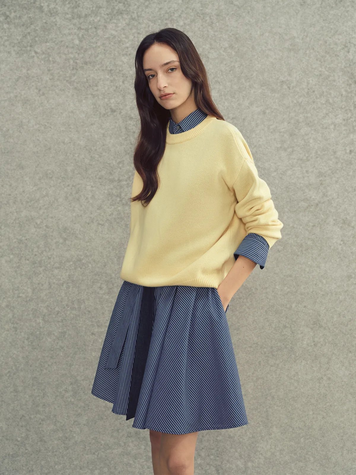Model in lemon JILL jumper layered over striped blue-and-white collared shirt with pleated navy mini skirt