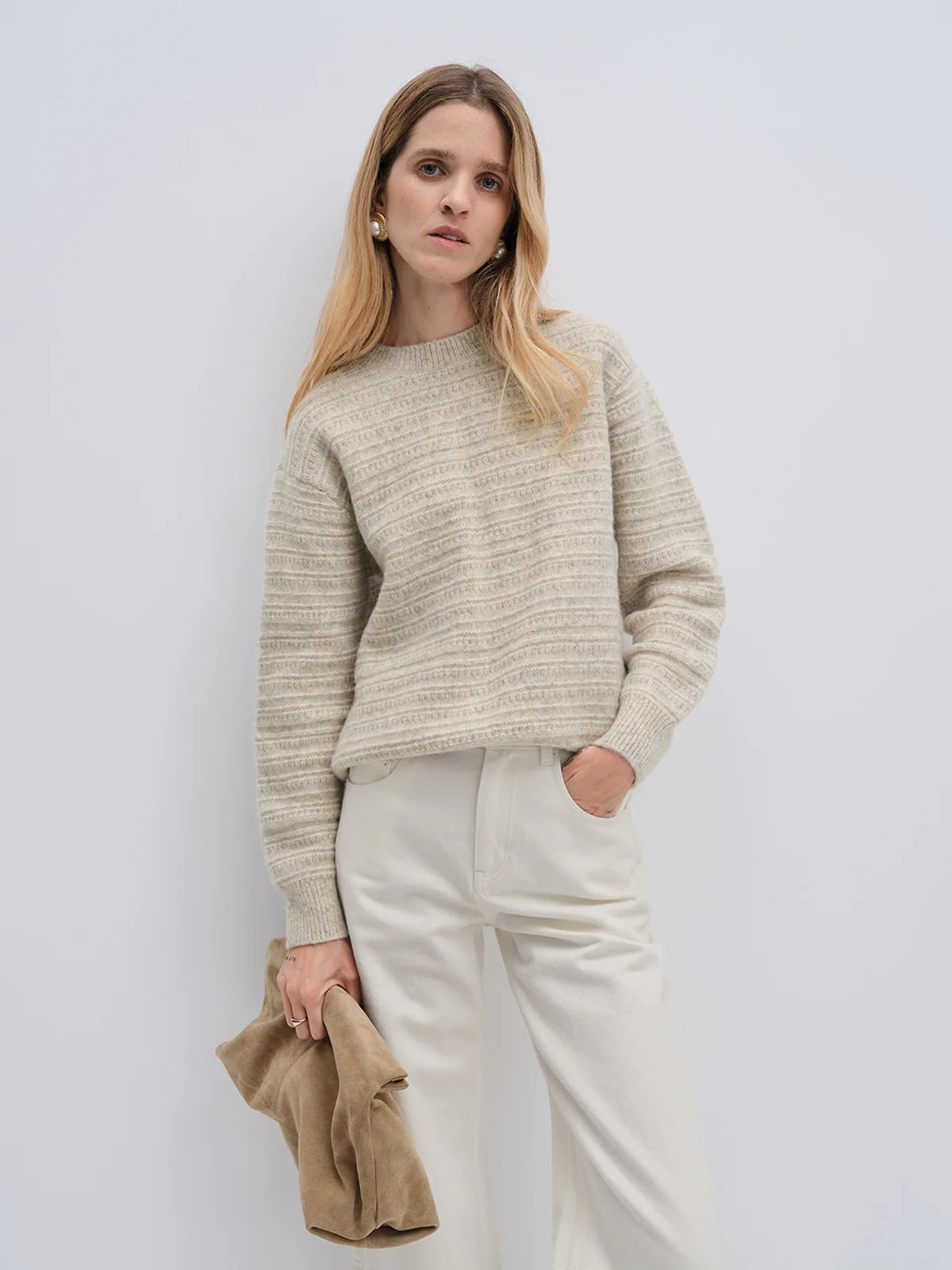 Front view of model in andreatang wool-cotton painterly stripe sweater with ivory trousers and suede clutch