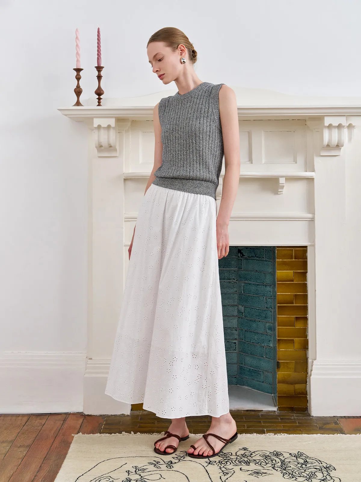 Model standing by white fireplace wearing grey MILLIE tank with white eyelet cotton maxi skirt — timeless minimalist ensemble