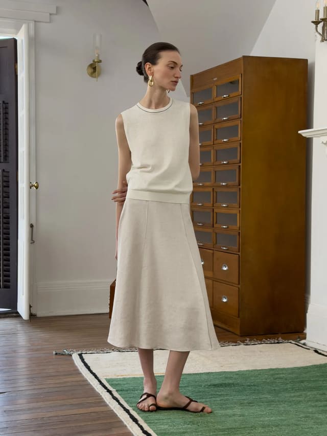 Model wearing ivory sleeveless knit top with A-line skirt in vintage-inspired interior setting