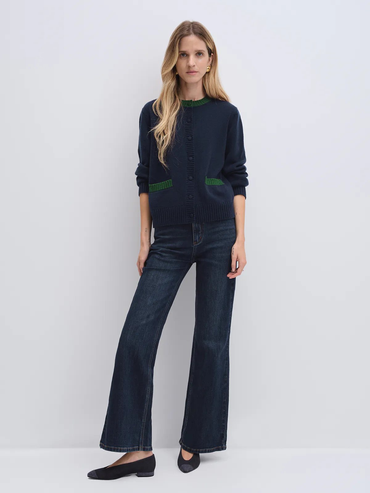 Front view of model in navy cardigan with contrast trim at collar and patch pockets, worn over light shirt with flared jeans.