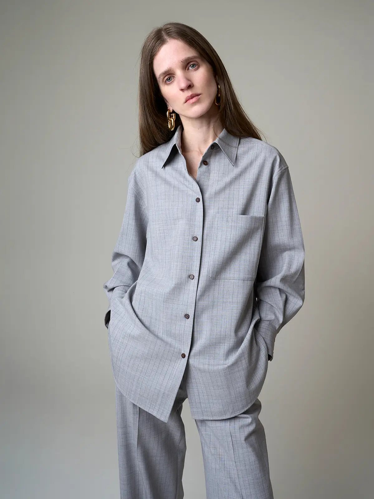 Front view of model in the grey striped loose wool shirt with hands in pockets, emphasizing oversized silhouette and button closure.