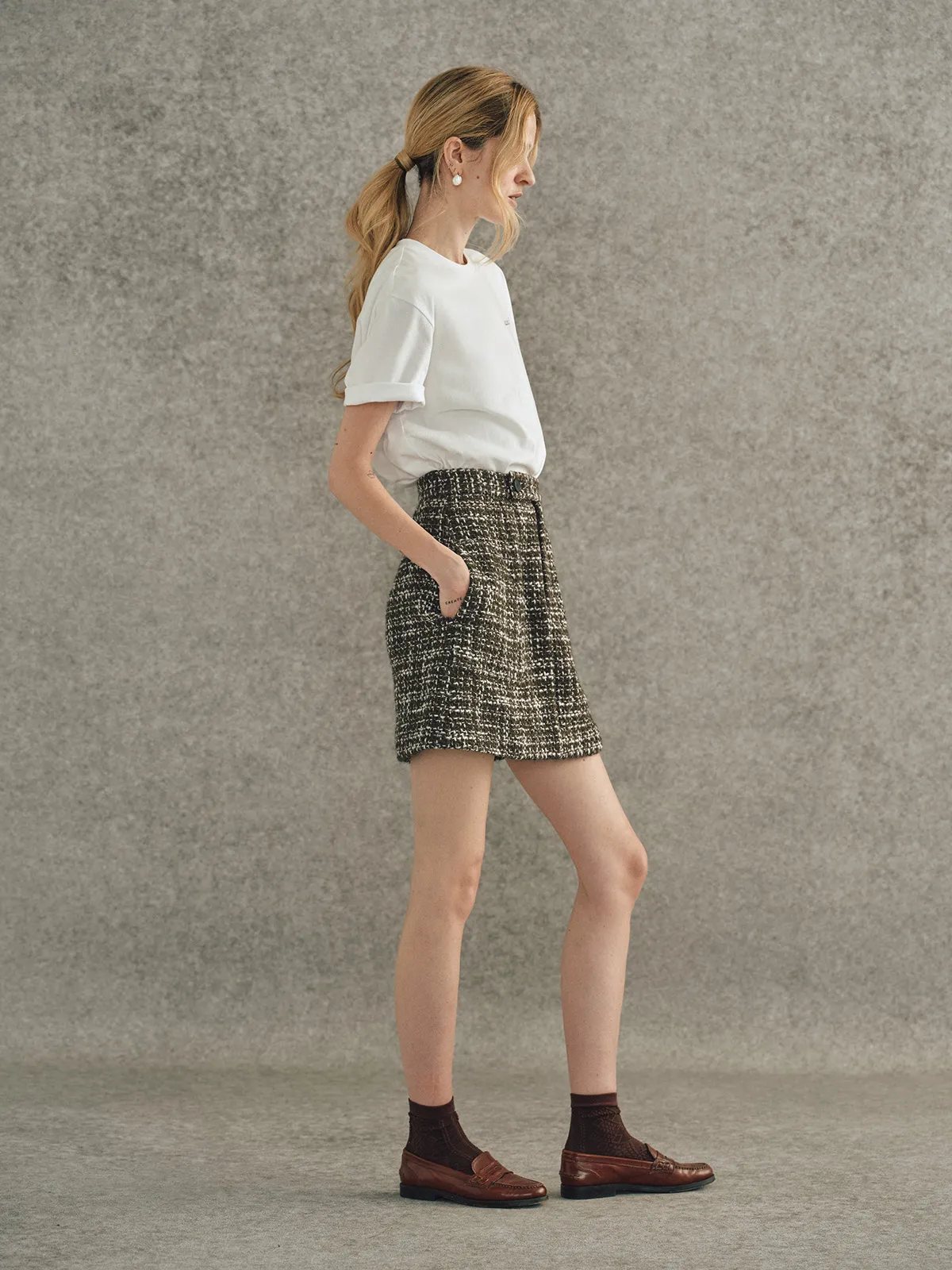 Side view of model wearing embroidered t-shirt with tweed skirt and brown loafers