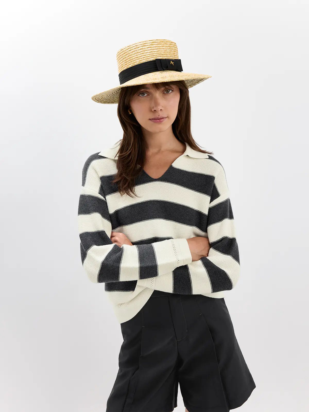Model wearing a Grey/White striped V-neck jumper with ribbed texture, tucked into white trousers and belted.