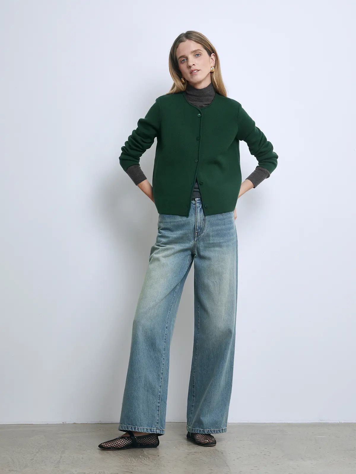 Front view of a model wearing a green button-front knit cardigan layered over a plaid shirt and skirt.