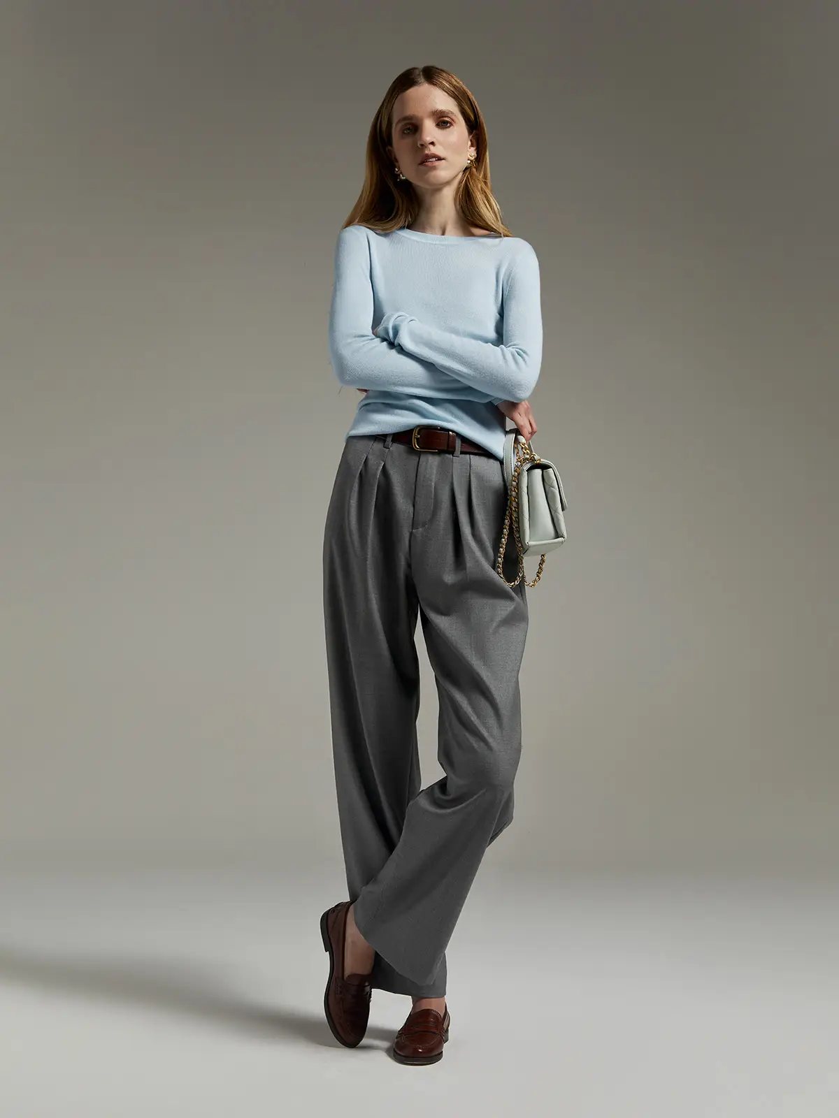 Model wearing Grey classic wool wide-leg trousers with pleats, light sweater, and belt, arms crossed.