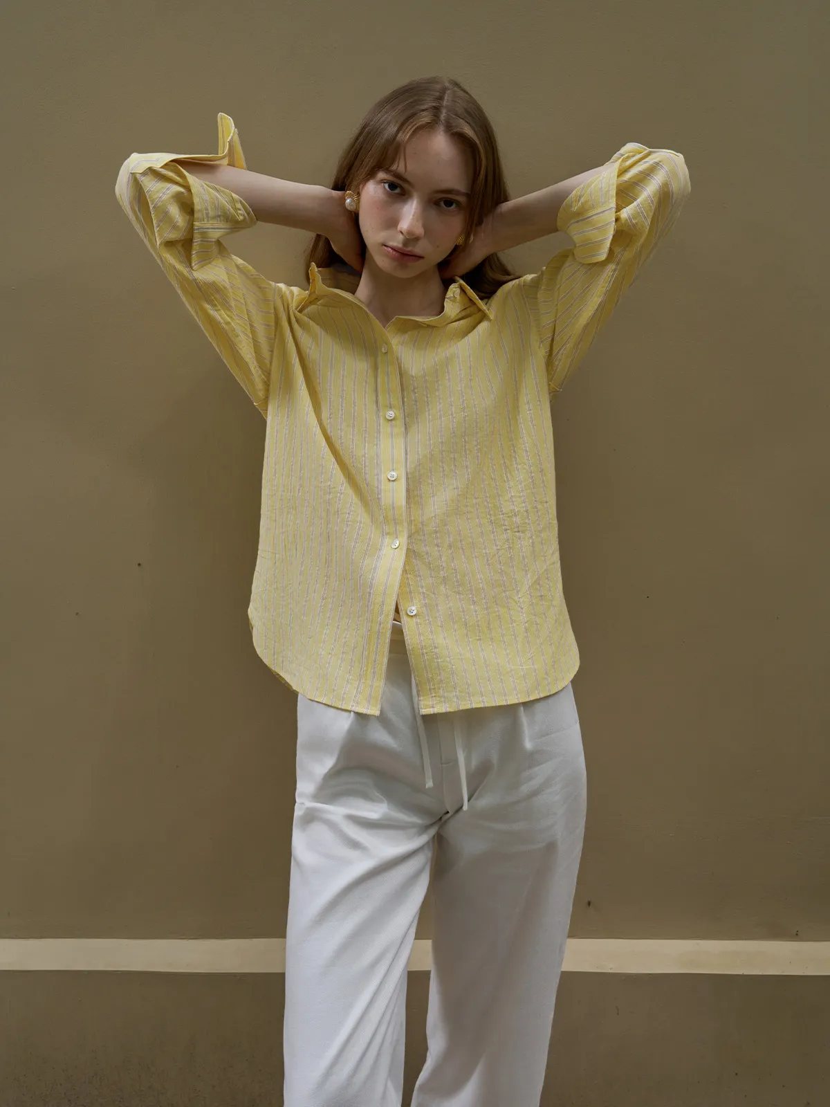 Model posing with hands behind head in buttercup shirt and white drawstring pants