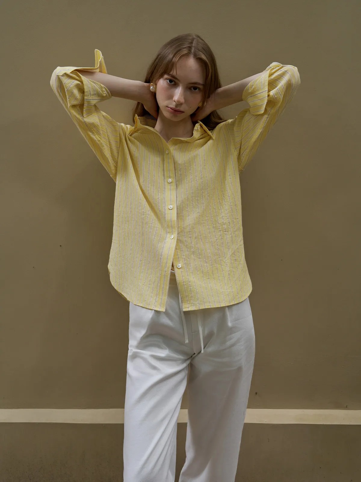 Model posing with hands behind head in buttercup shirt and white drawstring pants