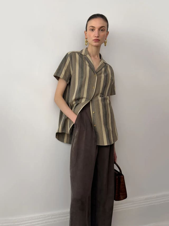 A model wearing a minimalist striped camp collar short-sleeve shirt paired with dark brown wide-leg trousers, representing a sophisticated quiet luxury aesthetic for an elevated everyday wardrobe.