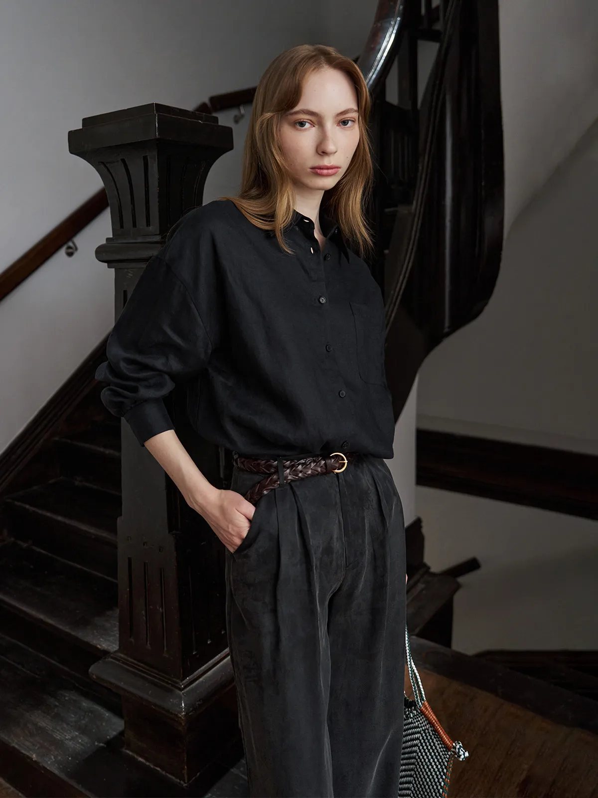 Model in black oversized shirt and charcoal trousers wearing PLAIT belt on ornate staircase
