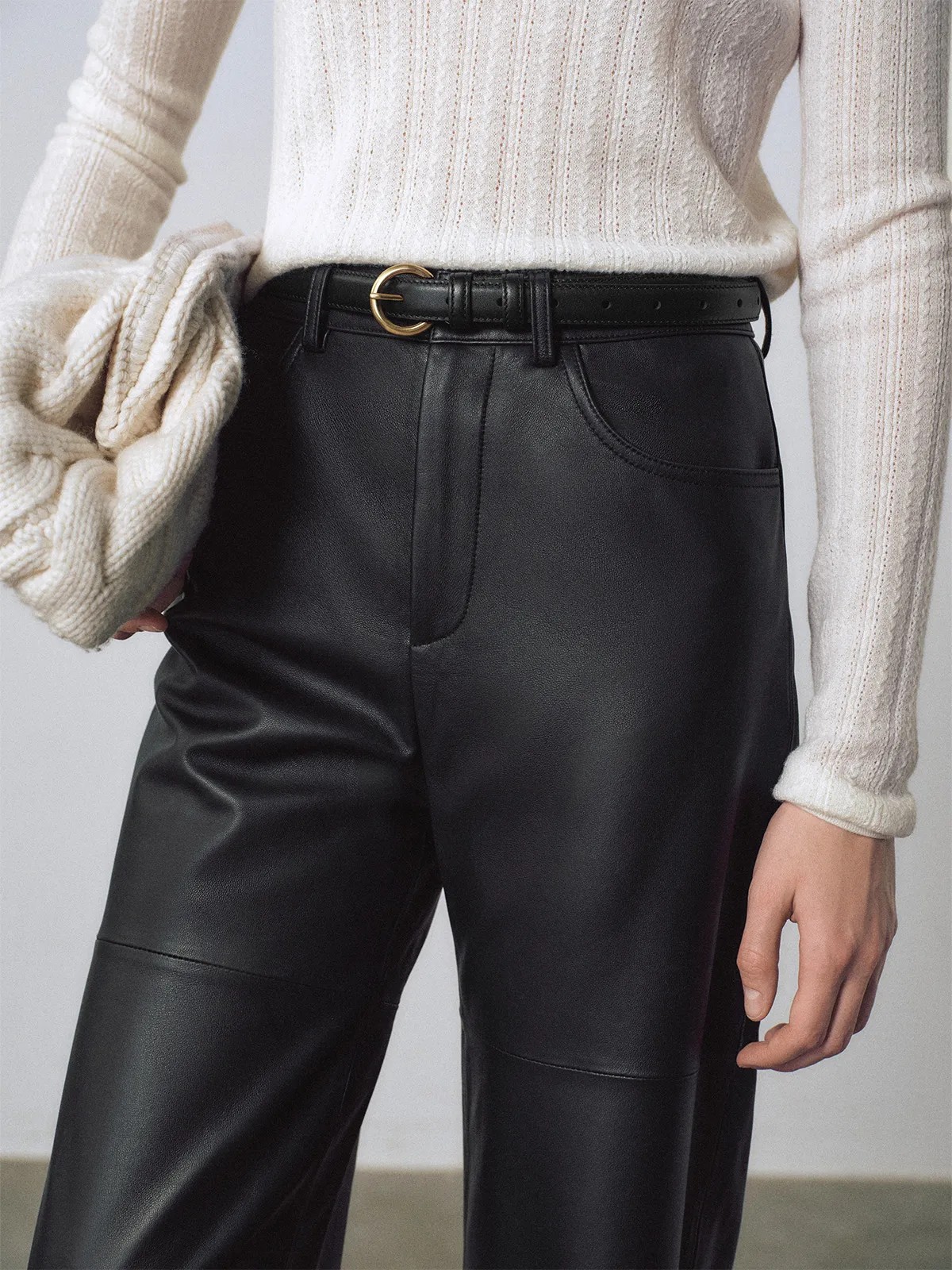 Woman wearing black KAY belt with gold buckle, paired with black leather trousers and ivory knit sweater