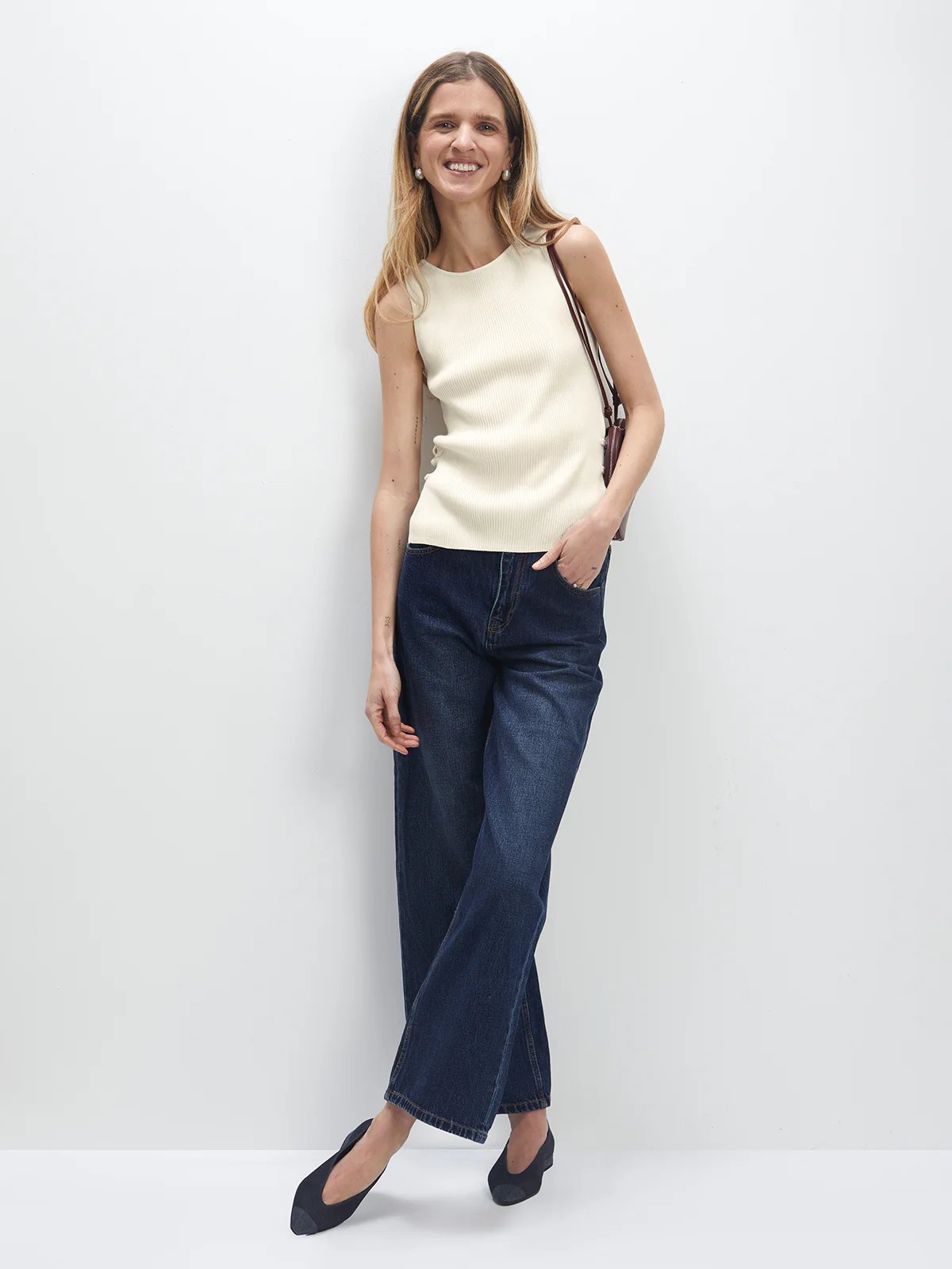 Model wearing blue wide-leg jeans with sleeveless top, one hand in pocket.
