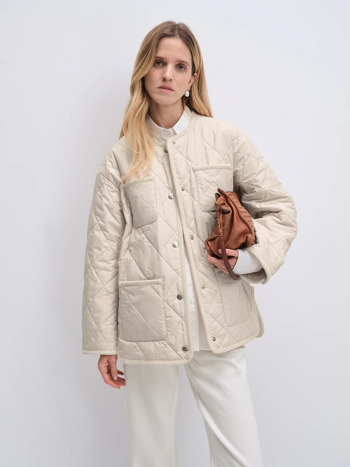 Model wearing off-white quilted textured jacket with button front and patch pockets, holding a woven bag.
