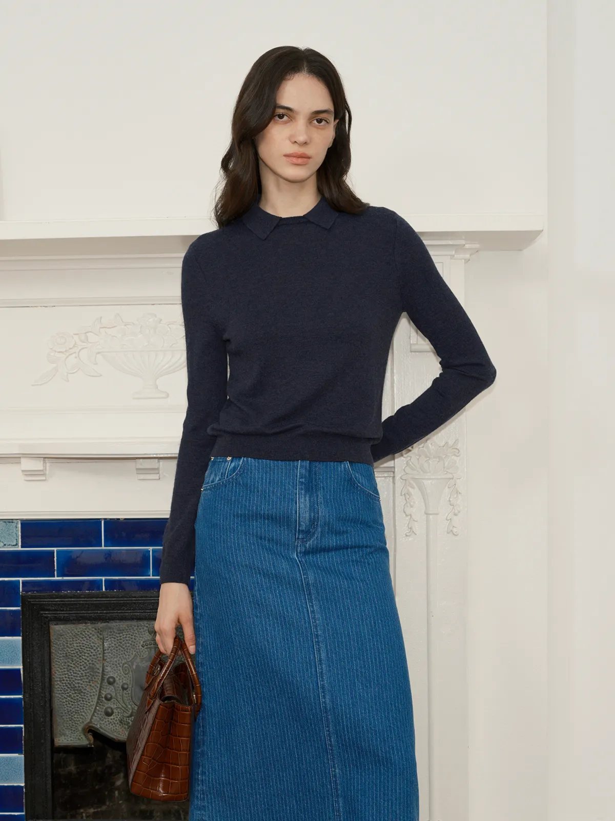 Model in navy LOUANE jumper with blue corduroy midi skirt and brown leather bag, hand on hip