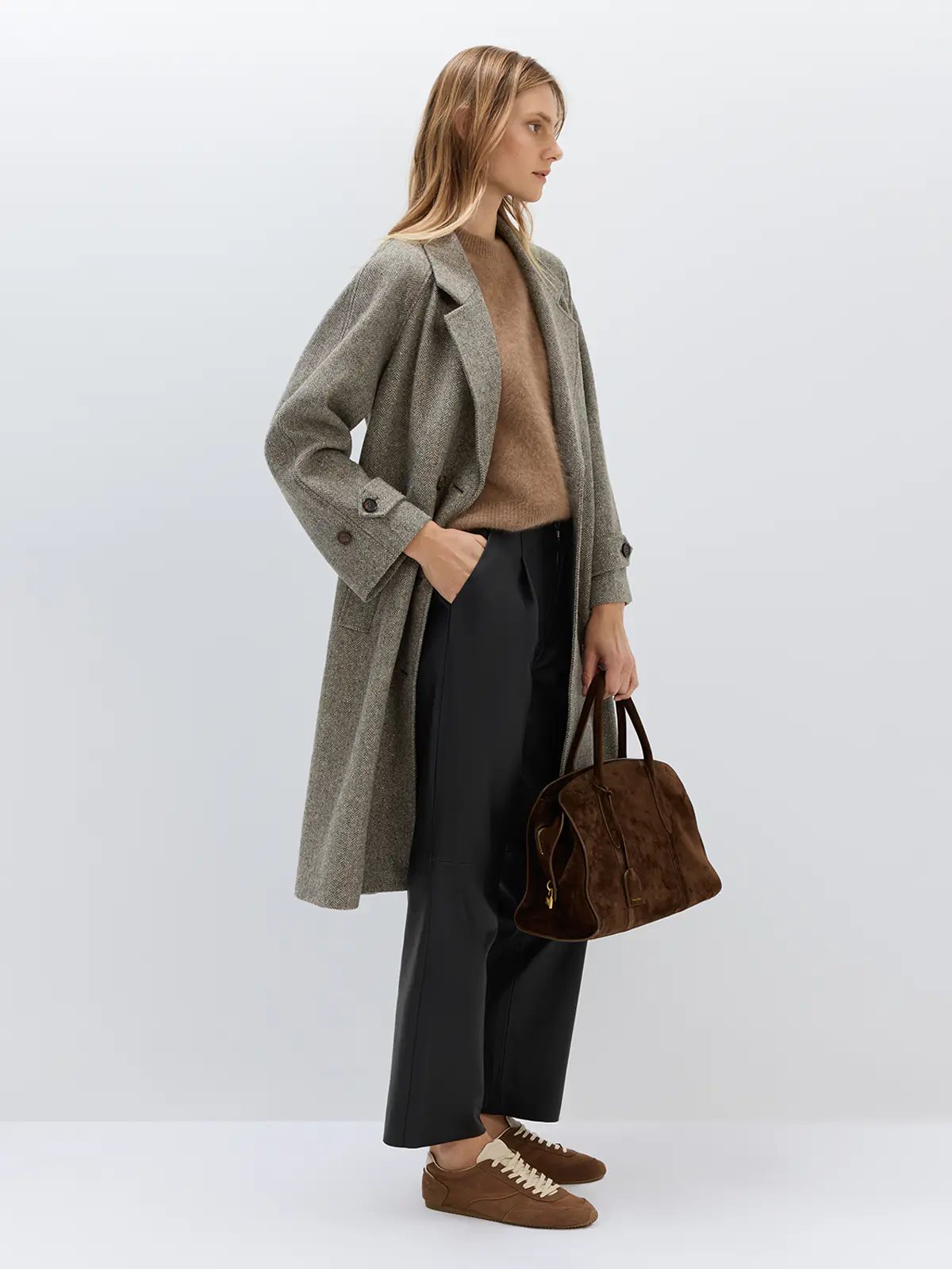 Side view of a brown herringbone double-breasted coat with structured shoulders and wide sleeves, paired with trousers.