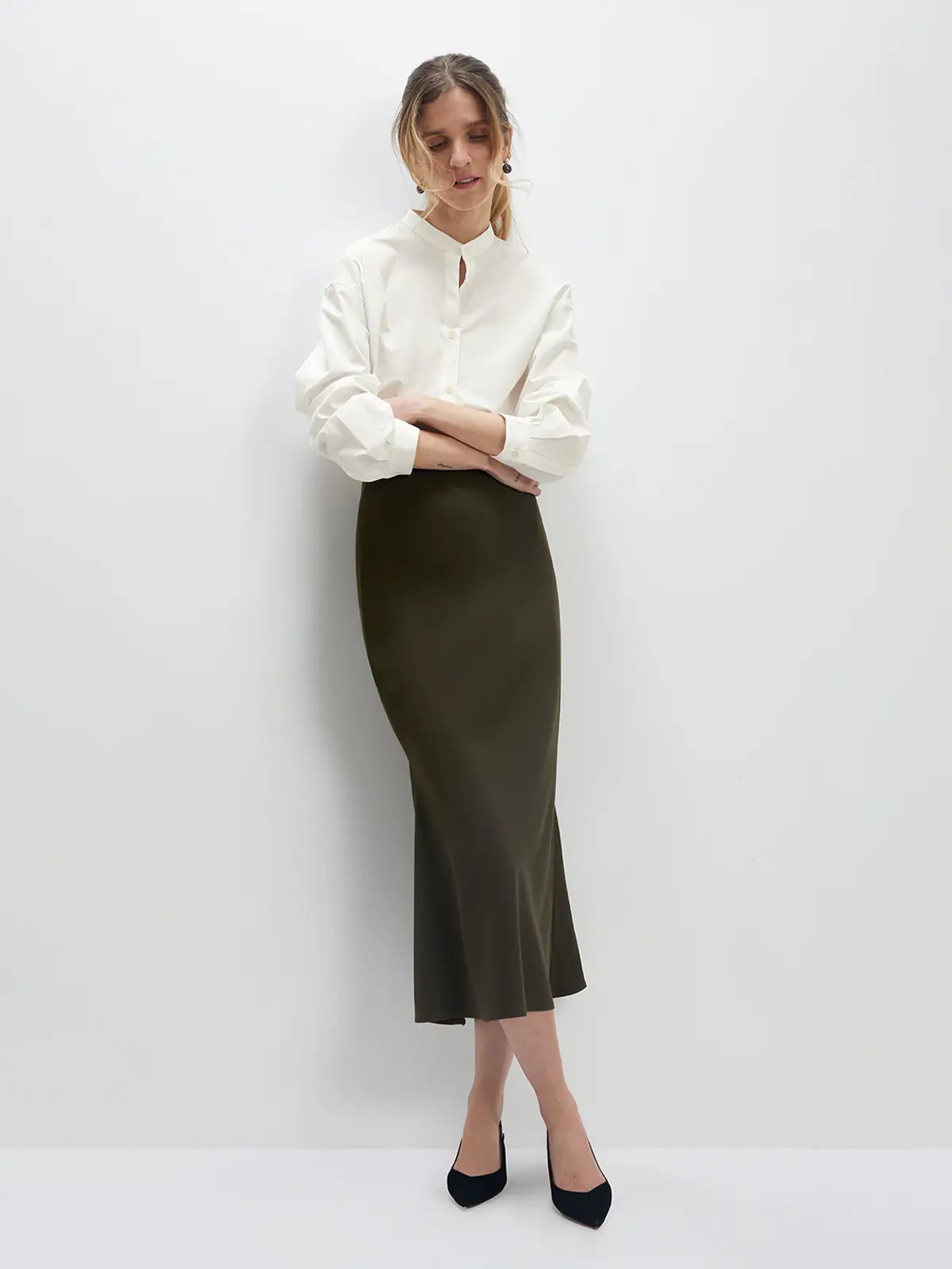 Model wearing an olive green acetate mermaid skirt with a blouse and heels, front view.