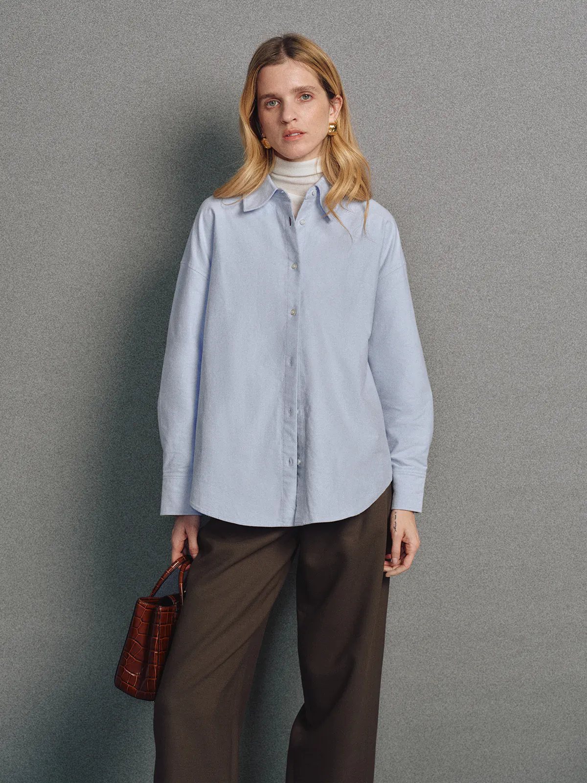 Side view of a model in a Blue brushed oxford shirt with contrast embroidery, worn over pants against a neutral backdrop.