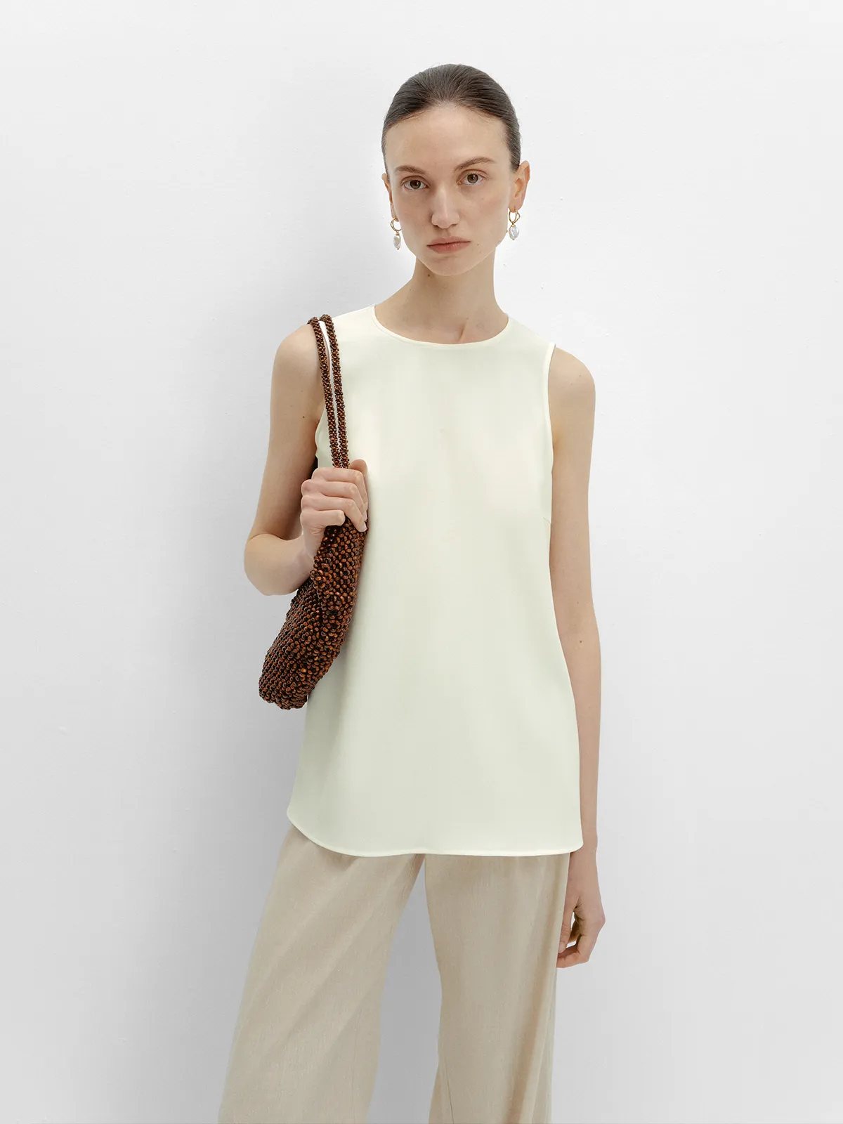 Model holding beaded brown clutch, wearing ivory MADGE blouse with beige wide-leg trousers and pearl drop earrings