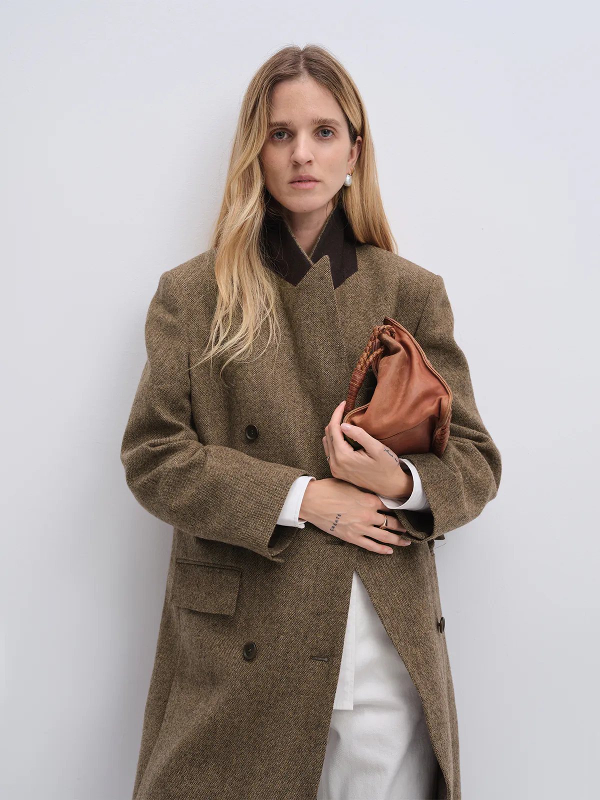 Front view of model wearing a brown wool and alpaca tweed long coat with double-breasted closure and notched lapels.