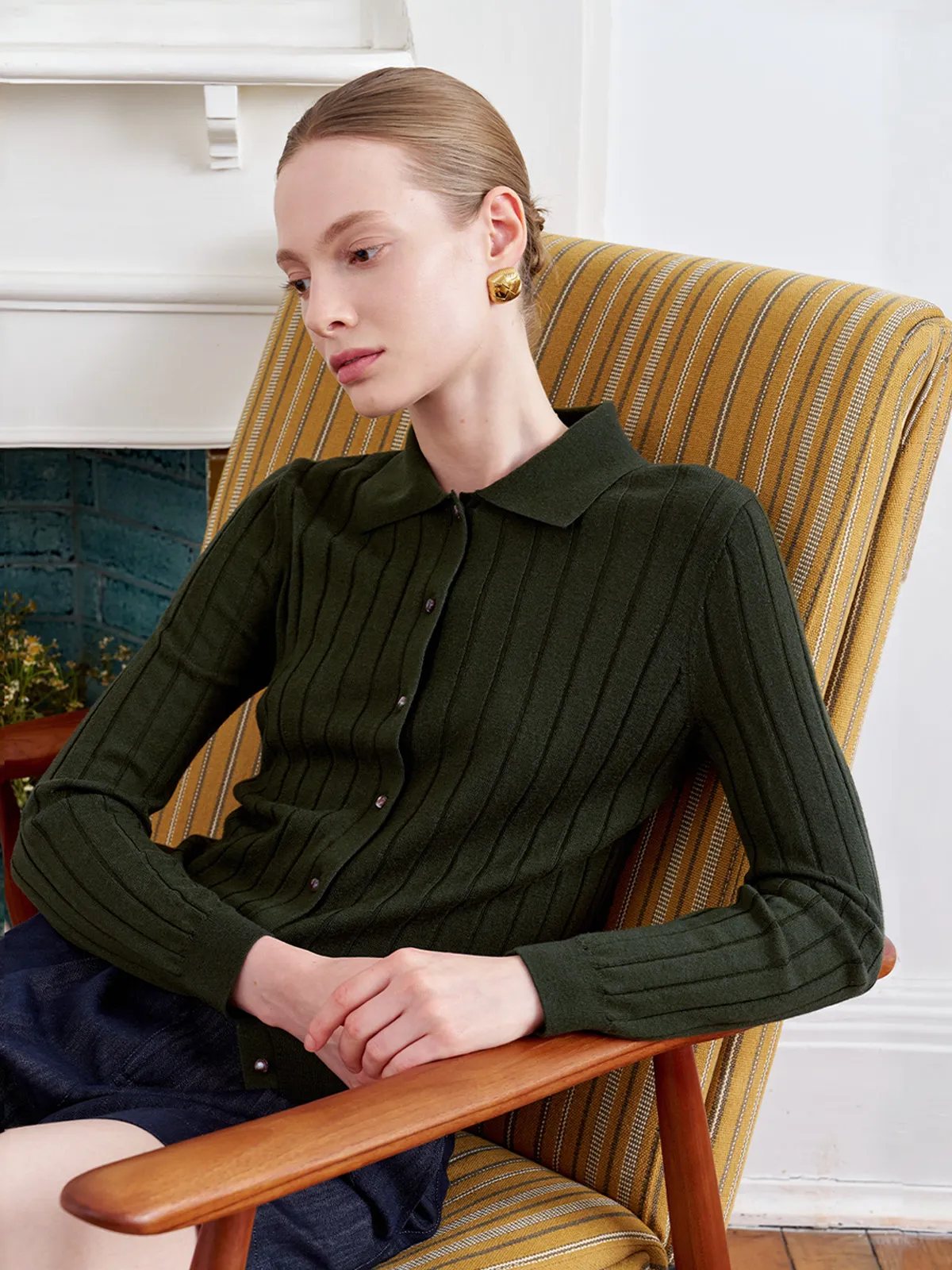 Model in forest green CONSTANCE cardigan seated on striped armchair