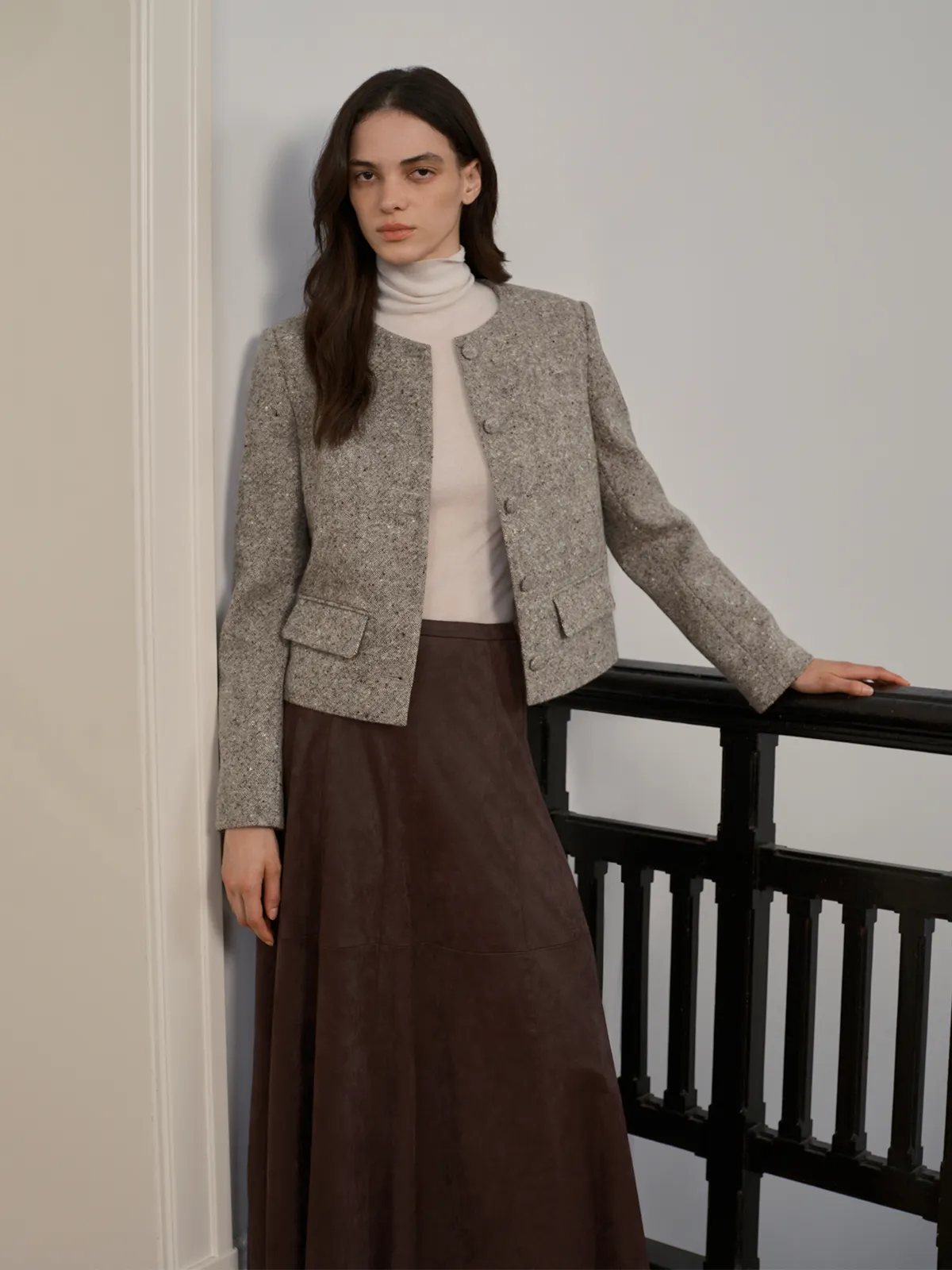 Three-quarter view of CLARKE jacket with brown suede skirt—model leaning on railing, showcasing sleeve and back drape