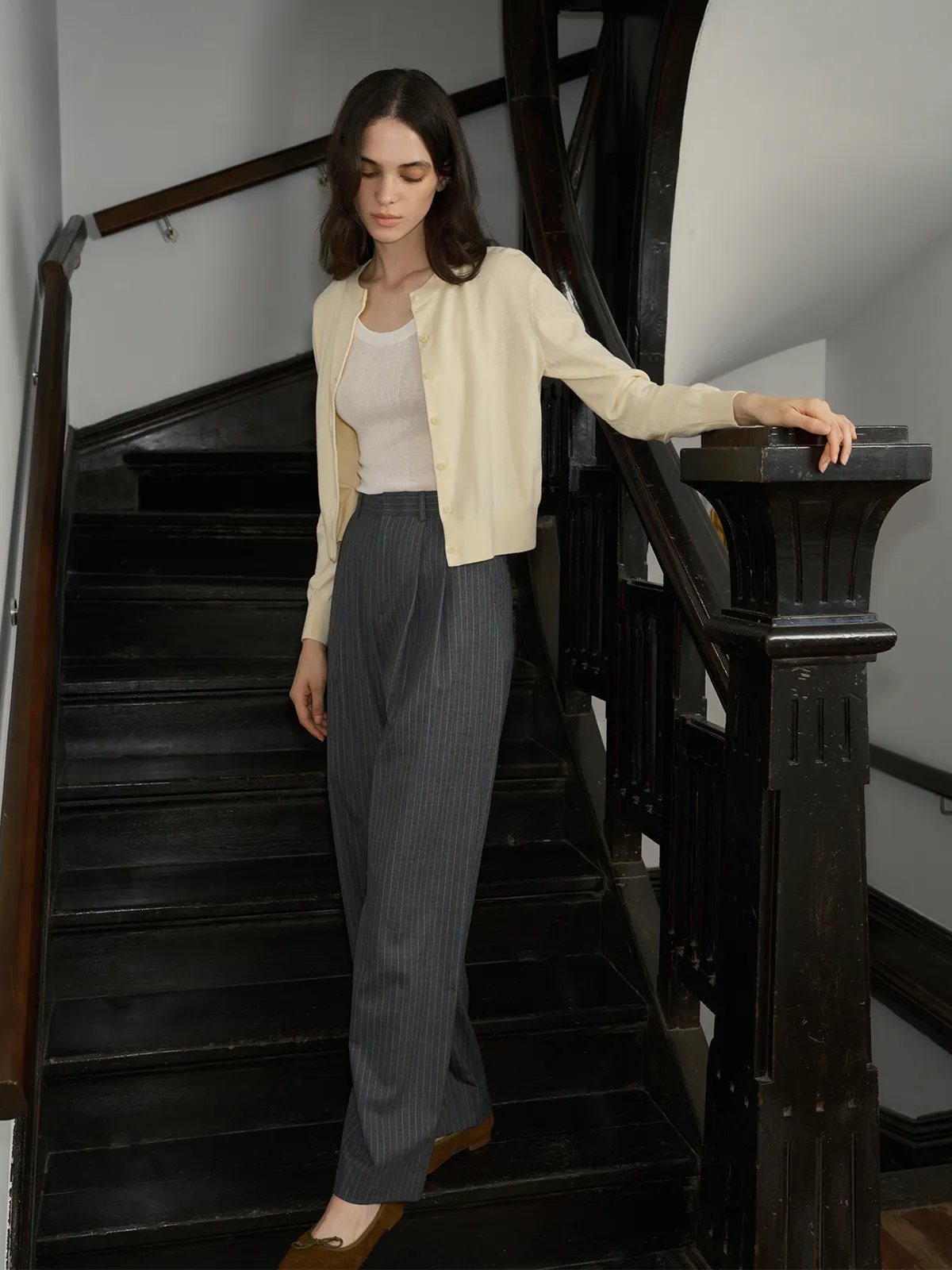 Model descending staircase in BINX cardigan, hand on banister, relaxed posture