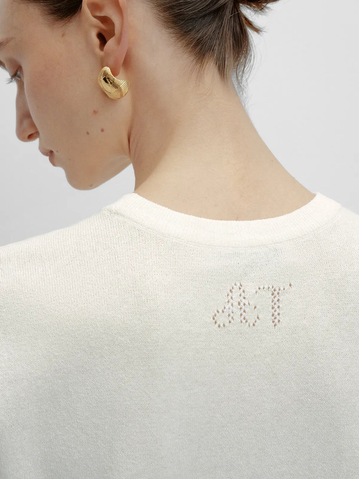 Back neckline detail of LIANA t-shirt showing subtle AT monogram knit logo, ivory fine-gauge knit